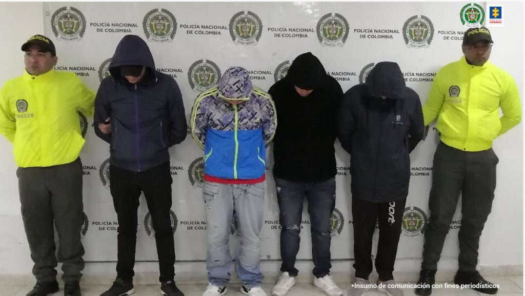 En la fotografía se observa a los cuatro capturados junto a dos agentes de la Policía Nacional. En la parte superior se observa un banner de la Policía Nacional