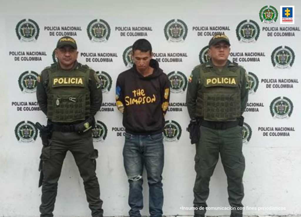 En la fotografía se observa al capturado junto a dos agentes de la Policía Nacional. En la parte superior se observan un banner de la Policía Nacional. 