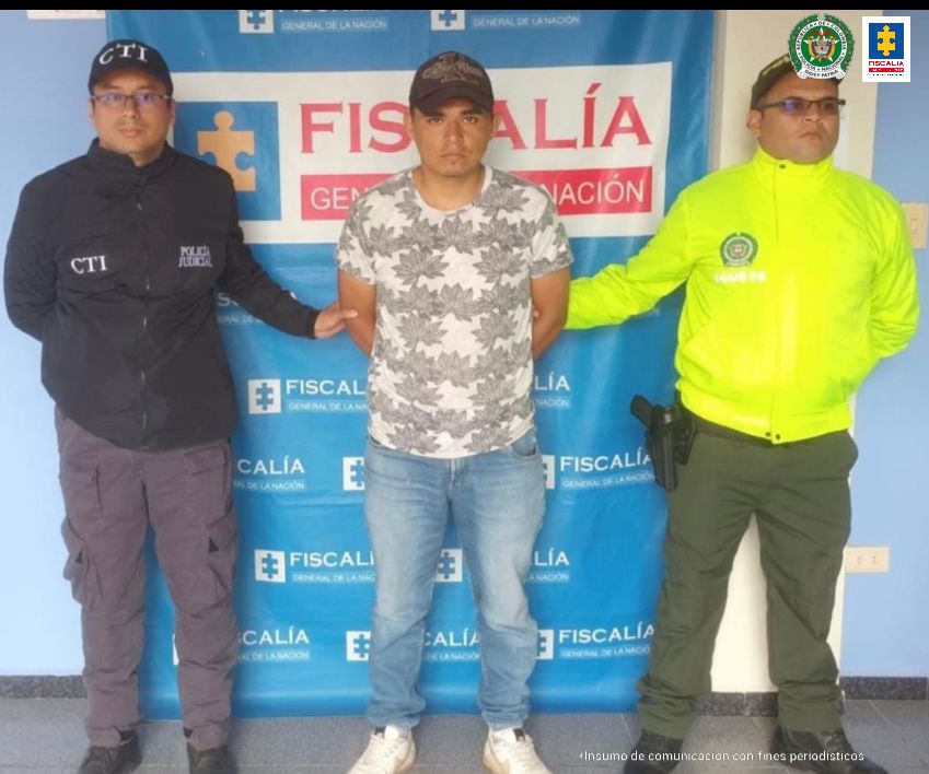 En la fotografía se observa al capturado junto a un servidor del CTI y un agente de la Policía Nacional. En la parte superior se observa un banner de la Fiscalía General de la Nación