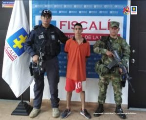 En la fotografía aparece el capturado junto a un servidor del CTI, y un soldado del Ejército Nacional. En la parte superior está un banner de la Fiscalía General 