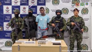 En la fotografía aparece el capturado junto a dos unidades de la Armada Nacional, del Ejército y el Gaula Mililtar y un agente del Goes de la Policía Nacional. En la parte posterior se observa una mesa con un fusil de asalto, proveedores y munición