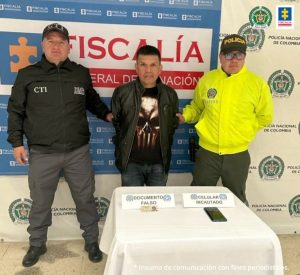En la fotografía aparece el capturado junto a un agente de la Policía Nacional y un servidor del CTI. En la parte superior está un banner de la Fiscalía General de la Nación
