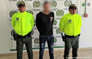 El capturado está esposado y custodiado por uniformados de la Policía Nacional.