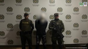 El capturado está esposado y custodiado por uniformados de la Policía Nacional.
