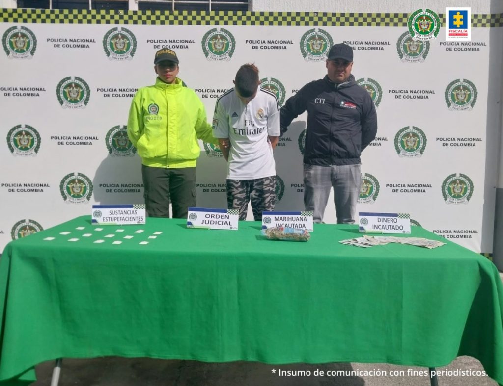 En la fotografía se aprecia, de pie, con los brazos atrás y la cabeza agachada a Mario Fernando Botero, alias Mister. Viste camiseta blanca con logos y pantalón camuflado. Al lado izquierdo de él hay un servidor del CTI de la Fiscalía y al lado derecho un uniformado de la Policía Nacional. Delante de ellos hay una mesa con mantel verde y sobre ella hay varias papeletas plásticas transparentes con contenido blanco y otra con contenido vegetal; asimismo, dinero en efectivo y cuatro letreros que dicen: ‘Sustancia estupefaciente’, ‘Orden judicial’, ‘Marihuana incautada’ y ‘Dinero incautado’. Detrás de ellos hay un pendón institucional de la Policía.
