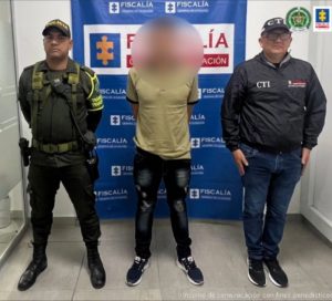en la imagen se ve una persona detenida bajo custodia del CTI y la Policía. Detrás suyo un backing de la Fiscalía.