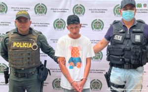 En la fotografía está el capturado junto a un servidor del CTI y un agente de la Policía Nacional. En la parte superior se observa un banner de la Policía Nacional