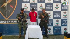 En la fotografía está el capturado junto a un agente de la Policía Nacional y un soldado del Gaula de la Armada Nacional. En la parte superior se observa un banner del Gaula Militar