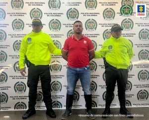 Se ve a alias El Paisa junto a dos policías a cada lado. En el fondo, se ve el backing de la Policía Nacional.