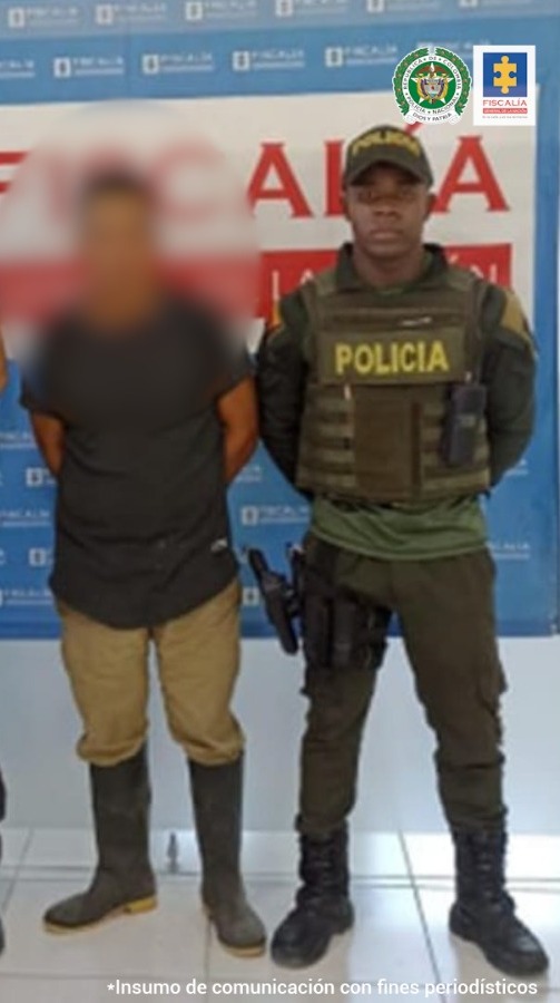 En la fotografía aparece el capturado junto con un servidor del CTI y un agente de la Policía Nacional. En la parte superior están un banner de la Fiscalía General