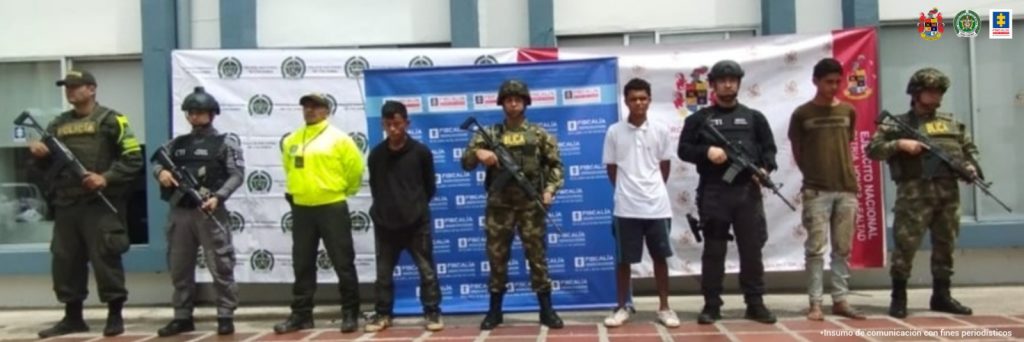 En la fotografía aparecen los tres capturados junto a dos agentes del Gaula de la Policía Nacional. En la parte superior está un banner del Ejército Nacional, un banner de la Fiscalía General y un banner de la Policía Nacional