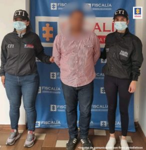 En la fotografía aparece el capturado junto a dos servidoras del CTI. En la parte superior está un banner de la Fiscalía General de la Nación
