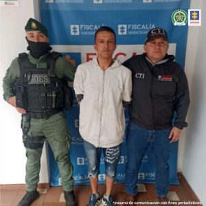 En la fotografía aparece el capturado junto a dos servidoras del CTI. En la parte superior está un banner de la Fiscalía General de la Nación