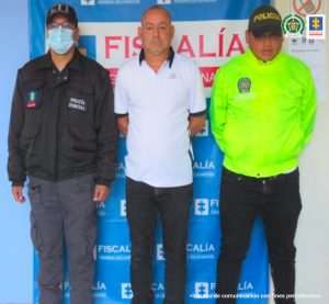 En la fotografía aparece el capturado junto a un servidor del CTI y un agente de la Policía Nacional. En la parte superior está un banner de la Fiscalía General de la Nación