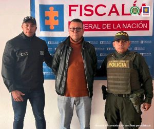 En la fotografía aparece el capturado junto a un servidor del CTI y un agente de la Policía Nacional. En la parte superior está un banner de la Fiscalía General de la Nación