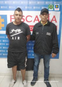 En la fotografía aparece el capturado junto a un servidor del CTI y un agente de la Policía Nacional. En la parte superior está un banner de la Fiscalía General de la Nación 