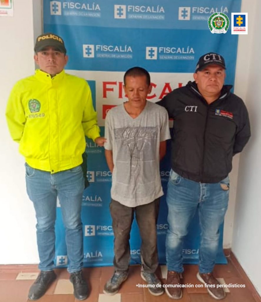 En la fotografía aparece el capturado junto a un servidor del CTI y un agente de la Policía Nacional. En la parte superior está un banner de la Fiscalía General de la Nación