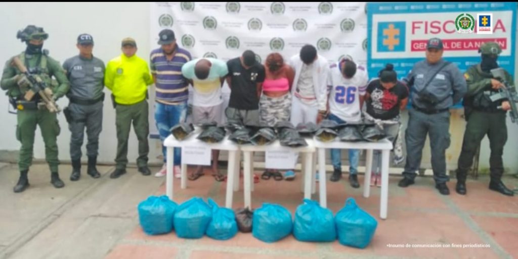 En las fotografías aparecen los asegurados junto a dos servidores del CTI y tres agentes de la Policía Nacional. En la parte posterior está una mesa con varias bolsas que contienen marihuana.