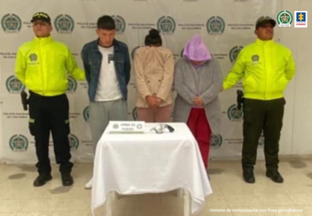 En la fotografía aparece el capturado junto a dos agentes de la Policía Nacional. En la parte posterior está una mesa con un arma de fuego con munición