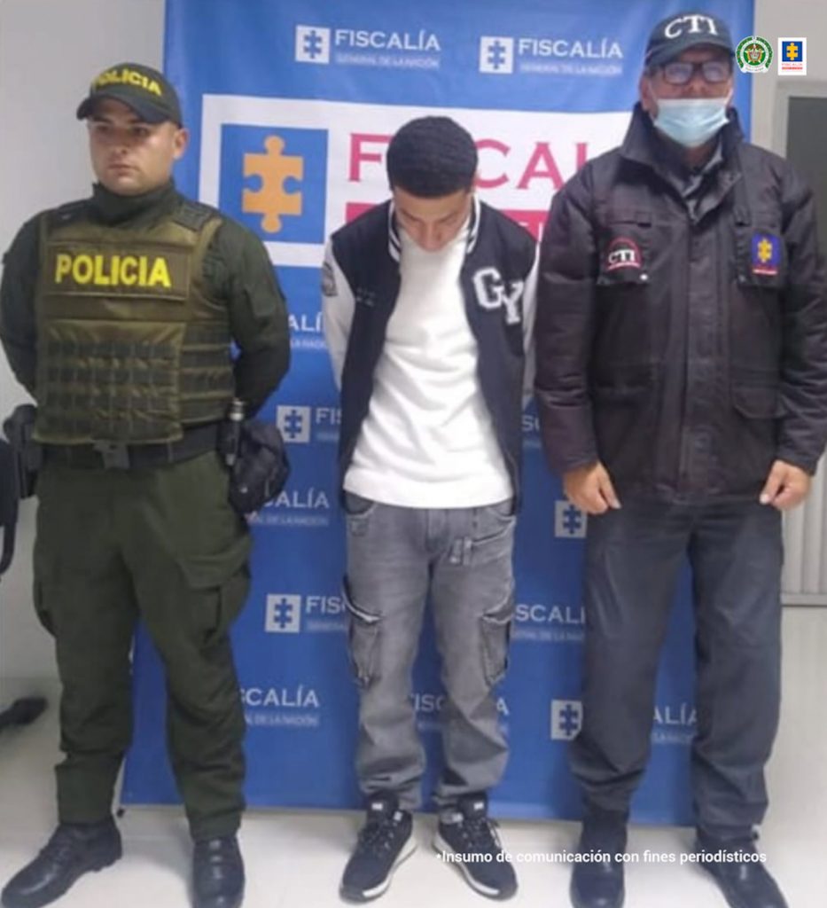 En la fotografía aparece el capturado junto a unaservidor del CTI y un agente de la Policía Nacional. En la parte superior está un banner de la Fiscalía General