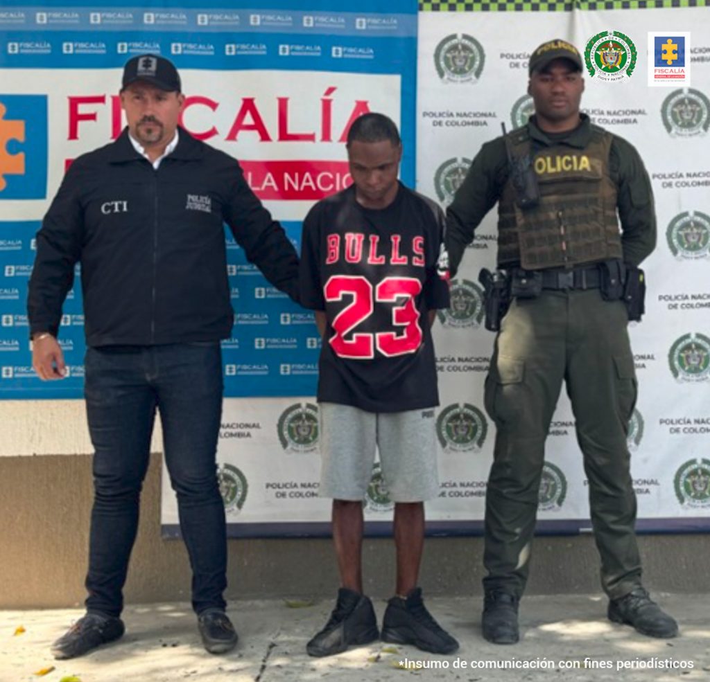 En la fotografía aparece el capturado junto a un servidor del CTI y un agente de la Policía Nacional. En la parte superior están un banner de la Fiscalía General y un banner de la Policía Nacional