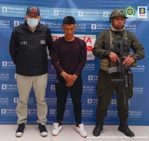 En la fotografía aparece el capturado junto a un servidor del CTI y un agente de la Policía Nacional. En la parte superior está un banner de la Fiscalía General de la Nación