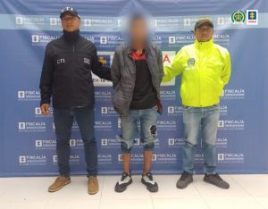 En la fotografía aparece el capturado junto a un funcionario del CTI y un agente de la Sijin de la Policía Nacional. En la parte superior está un banner de la Fiscalía General