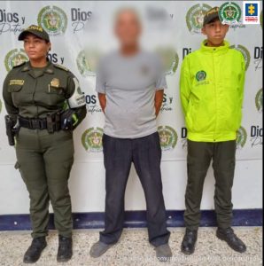 En la imagen aparece un hombre de suéter gris entre dos uniformados de la Policía.