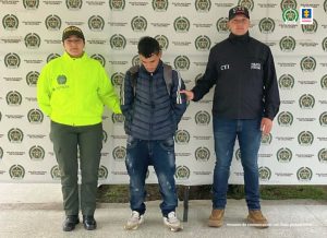 En la fotografía aparece el capturado junto a un servidor del CTI y una agente de la Policía Nacional. En la parte superior está un banner de la Policía Nacional