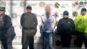 Se visualiza al investigado junto a una investigadora del CTI y uniformados de la Policía y Ejército Nacional. Detrás de ellos el banner institucional de la Policía Nacional.