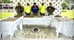En la fotografía aparece el capturado junto a un a dos agentes de la Policía Nacional. En la parte posterior están tres mesas con munición de diferentes calibres, tres armas de fuego, teléfonos celulares y dinero en efectivo