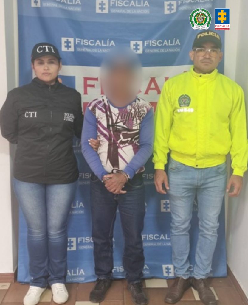 En la fotografía aparecen el capturado junto a una servidora del CTI y un agente de la Policía Nacional. En la parte superior está un banner de la Fiscalía General de la Nación