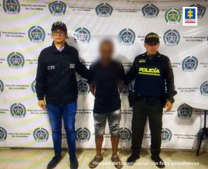 En la fotografía aparecen el capturado junto a un funcionario del CTI y un agente de la Policía nacional. En la parte superior está un banner de la Policía Nacional