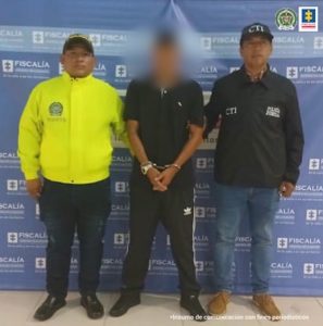 En la fotografía aparece el capturado junto a un servidor del CTI y un agente de la Policía Nacional. En la parte superior está un banner de la Fiscalía General de la Nación
