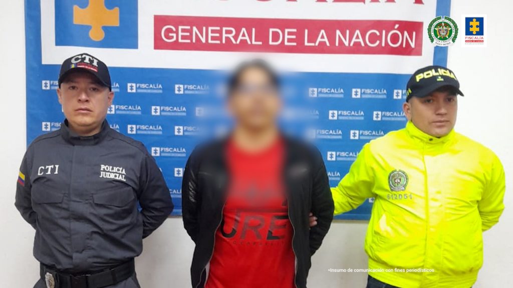 En las fotografía aparece el capturado junto a un servidor del CTI y un agente de la Policía Nacional. En la parte superior está un banner de la Fiscalía General de la Nación