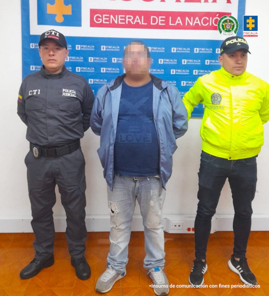 En la fotografía aparece el capturado junto a un servidor del CTI y un agente de la Policía Nacional. En la parte superior está un banner de la Fiscalía General de la Nación