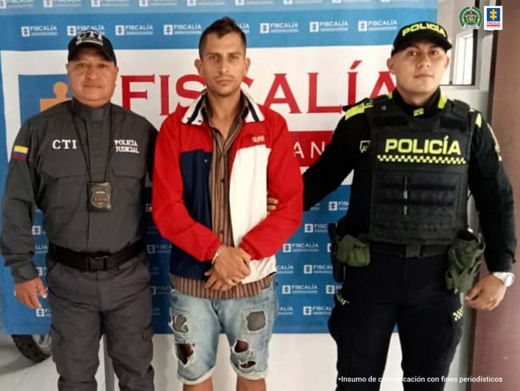 En la fotografía aparece el capturado junto a un servidor del CTI y un agente de la Policía Nacional. En la parte superior está un banner de la Fiscalía General de la Nación