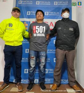 En la fotografía aparece el capturado junto a un servidor de CTI y un agente de la Policía Nacional. En la parte posterior está un banner de la Fiscalía General de la Nación