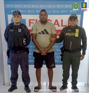 En la fotografía aparece el capturado junto a un funcionario del CTI y un agente de la Policía Nacional. En la parte superior está un banner de la Fiscalía General de la Nación