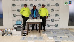 Capturado con esposas junto a dos uniformados de la Policía y al fondo un banner de la Policía Nacional