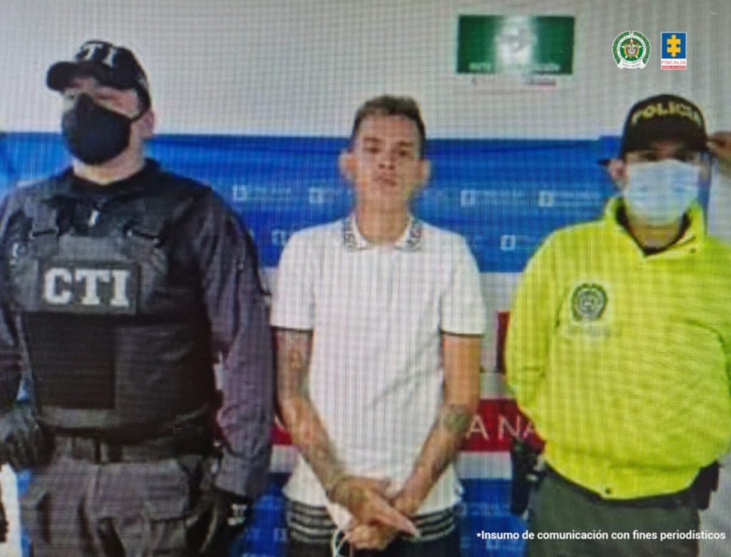 Se visualiza al capturado junto a un investigador del CTI y de la Policía Nacional. Detrás de ellos el banner que identifica a la Fiscalía General de la Nación.