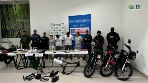 En la imagen se ven a tres hombres y una mujer capturados, quienes son custodiados por 6 uniformados del Cuerpo Técnico de Investigación (CTI) y la Policía Nacional. A su alrededor se observan elementos incautados por las autoridades como 4 motocicletas, autopartes, celulares, letras de cambio, y equipos de cómputo.