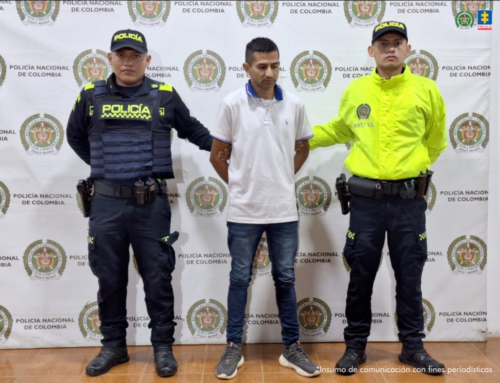 En la foto se ve al presunto delincuente en medio de dos agentes de policía, atras de ellos se ve un baking de la Policía