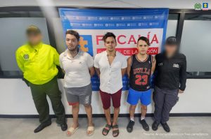Se observa a los capturados junto a un uniformado de la Policía Nacional y un investigador del CTI. Detrás de ellos el banner que identifica a la Fiscalía General de la Nación.