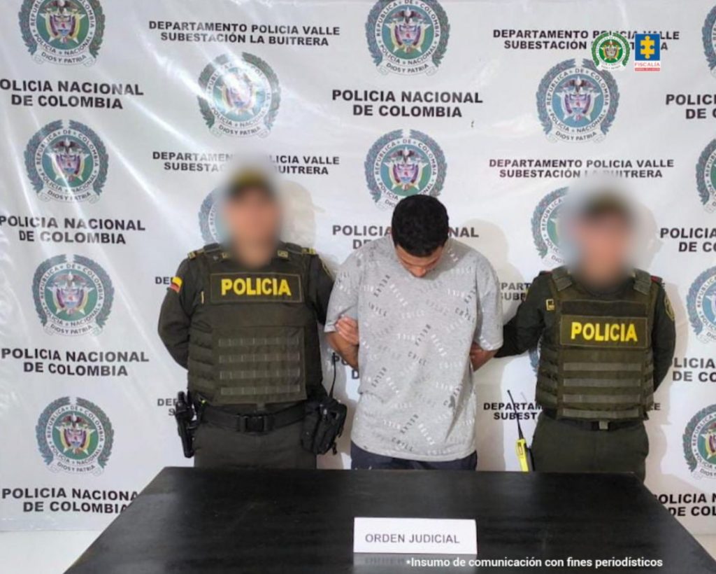 Se visualiza al capturado junto a dos uniformados de la Policía Nacional. Detrás de ellos el banner que identifica a la Policía Nacional
