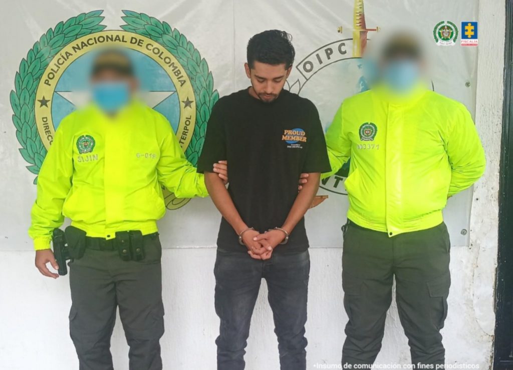 Se visualiza al capturado junto a dos uniformados de la Policía Nacional. Detrás de ellos se observa el banner de la Policía Nacional.