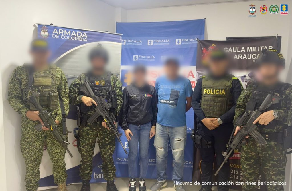Se observa al capturado con el rostro difuminado junto a un investigador del CTI y uniformados de la Armada, Ejército y Policía Nacional: Detrás de ellos los banners que identifican a la Fiscalía General de la Nación, Armada Nacional y Gaula Militar.