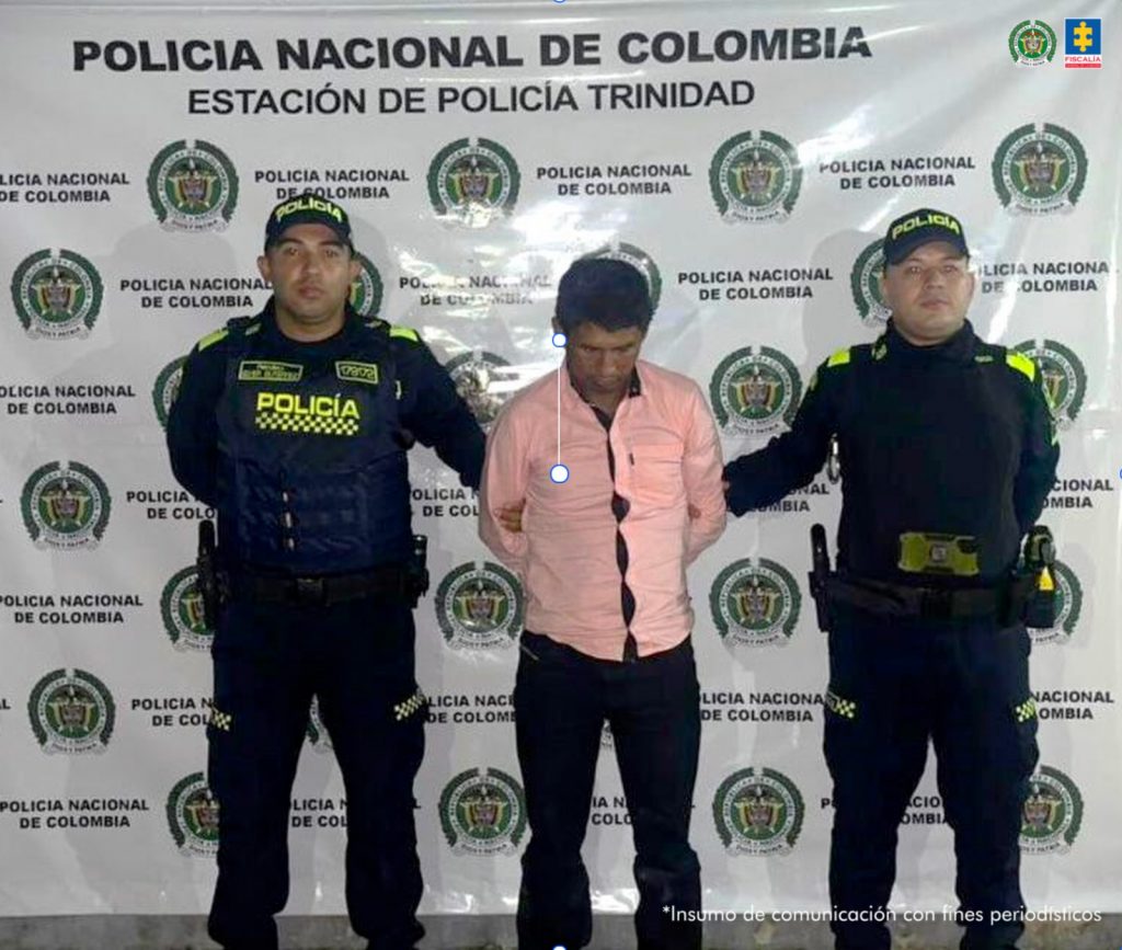 El capturado está esposado, y custodiado por dos uniformados de la Policía Nacional.