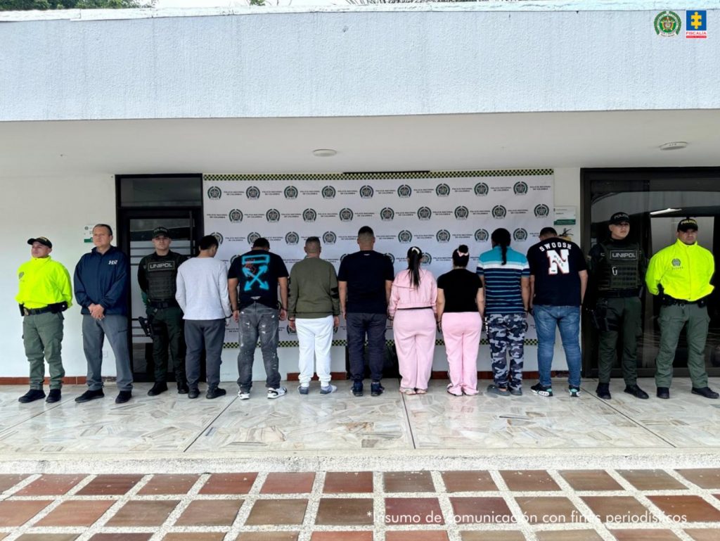 en la imagen se pueden ver los 8 capturados entre 4 funcionarios de la policia, detras de ellos hay un bakinf de la policia