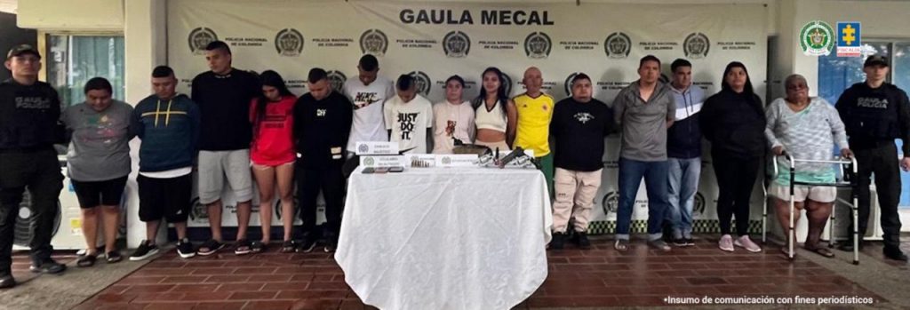 En la fotografía aparecen de pie presuntos integrantes del grupo delincuencial La 19 y otros procesados capturados en flagrancia. A sus extremos hay uniformados de la Policía Nacional. Delante de ellos hay una mesa y sobre ella hay celulares, munición, armas de fuego y otros elementos. Detrás, hay un pendón institucional de la Policía que dice: ‘Gaula Mecal’.
